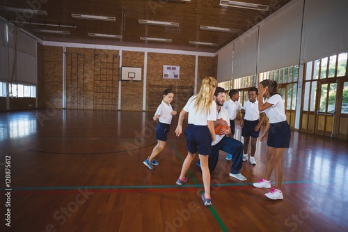 Sports teacher and school kids playing basketball