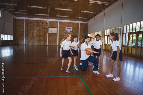 Sports teacher teaching school kids to play basketball