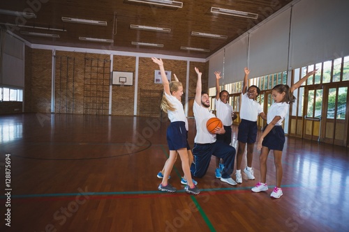 Sports teacher and school kids playing in basketball court