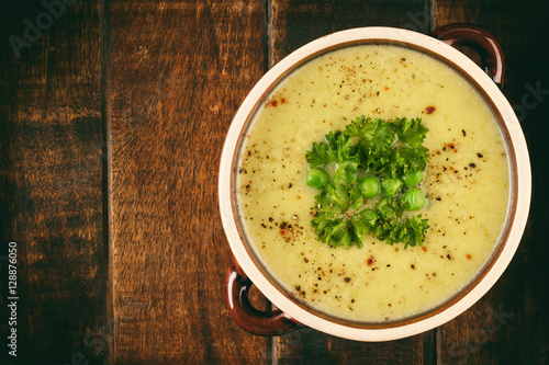  Cream soup with potatoes, leek and peas on wooden table.