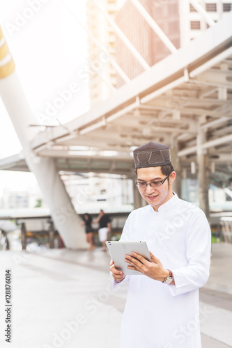 Young handsome businessman Arab Muslims looking at his business report in his tablet by internet network while standing at central of city. Business and technology concept.