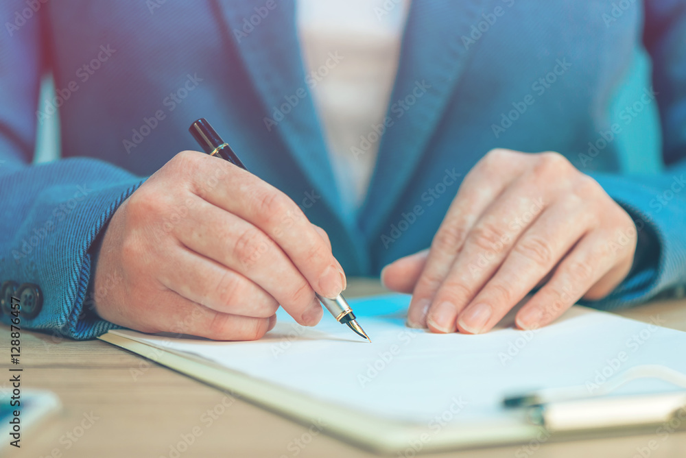 Close up of female hands writing signature on business agreement Close up of female hands writing signature on business agreement