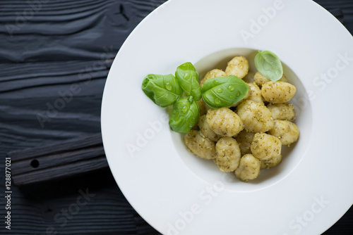 White plate with gnocchi and pesto on a black wooden surface
