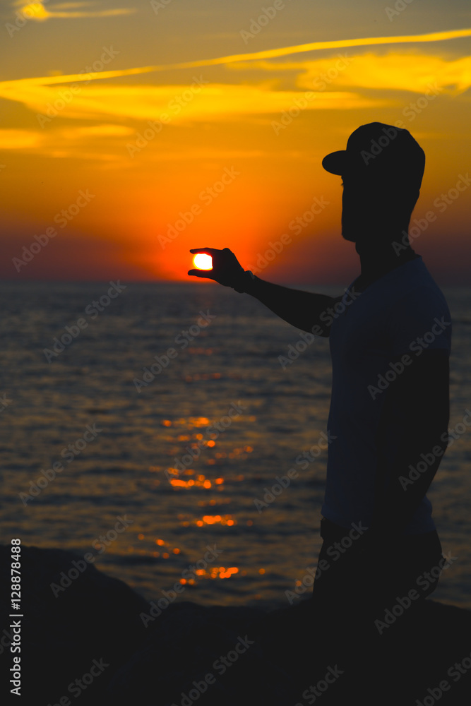 Silhouette of a man is holding the sun against the sunset.