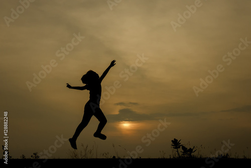Silhouette image of a girl jumping on the road with a sunset background.