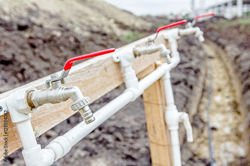 Few red taps are placed on plastic pipeline attached on wooden c