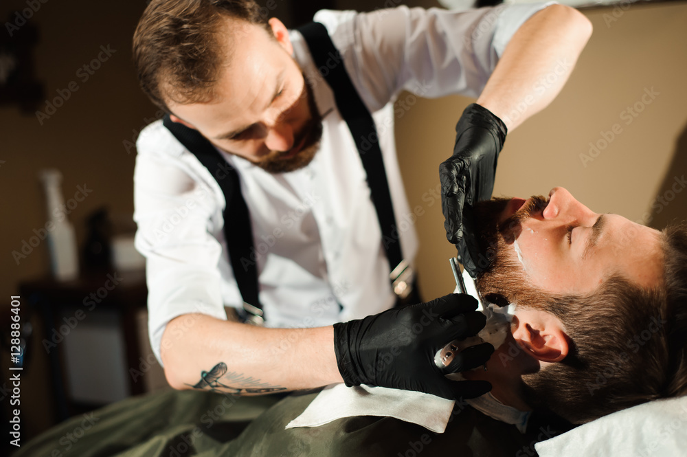 Naklejka premium Master cuts hair and beard of men in the barbershop