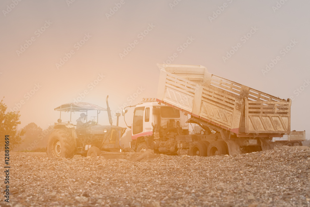 Fototapeta premium Dump truck with tractor dumping gravel on an excavation site