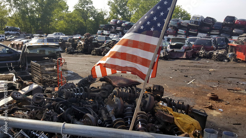 American Flag flying above a junk yard. Scrap vehicles