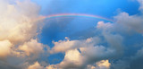 Bright rainbow in clouds at sunset panorama.