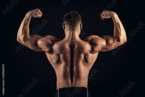 Rear view of healthy muscular young man with his arms stretched out isolated on black background © satyrenko