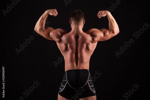 Rear view of healthy muscular young man with his arms stretched out isolated on black background © satyrenko