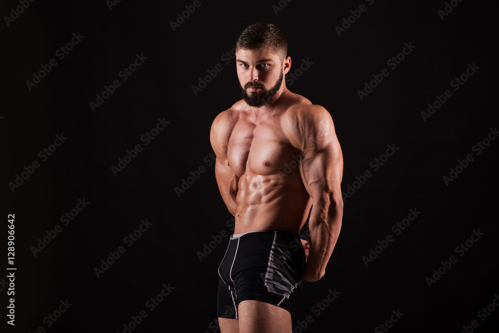 Fototapeta premium Handsome muscular bodybuilder posing over black background.