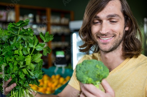 Happy man holding broccoli and bunch of herbs 