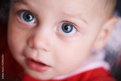 Cute baby looking straight up into the camera above him, shot very close up while he wears a red outfit for christmas.
