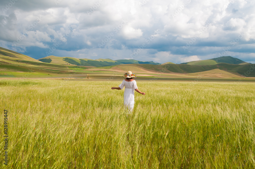 Girl in White dress and straw hat walking among fields in countryside Girl in White dress and straw hat walking among fields in countryside