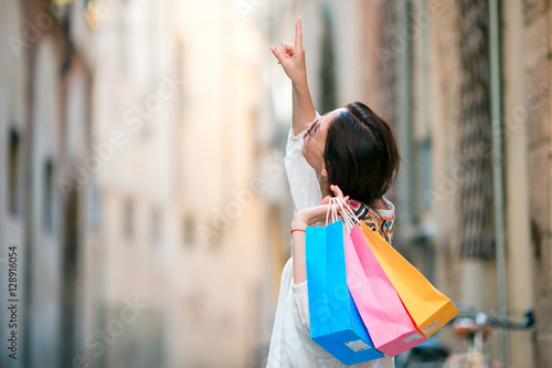 Young girl with shopping bags on narrow street in Europe. Portrait of a beautiful happy woman holding shopping bags smiling