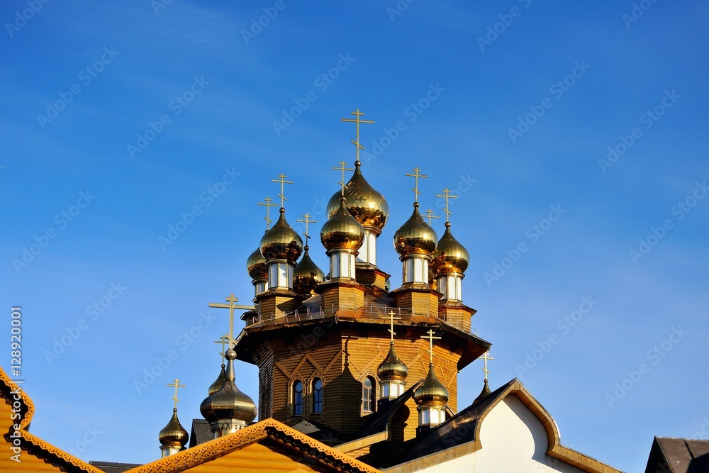 Wooden Church with Golden domes was consecrated by the sun against a blue sky background. Russia, Belgorod. Landscape orientation