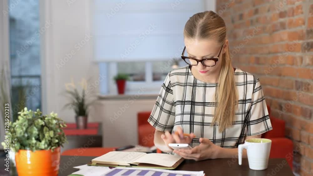 Girl looking on her smartphone and doing notes while sitting by the table
Girl looking on her smartphone and doing notes while sitting by the table