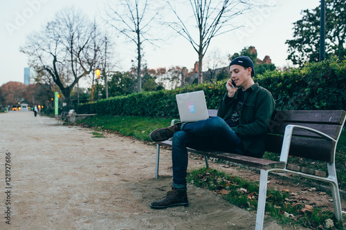 A man working on his laptop and talking on the phone in the park