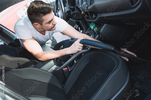 Mature man cleaning with vacum cleaner interior of luxury car.