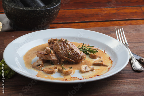 Concept: restaurant menus, healthy eating, homemade, gourmands, gluttony. White plate of pork medallions with mushroom sauce on weathered wooden table.