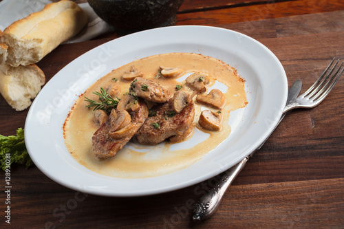 Concept: restaurant menus, healthy eating, homemade, gourmands, gluttony. White plate of pork medallions with mushroom sauce on weathered wooden table.