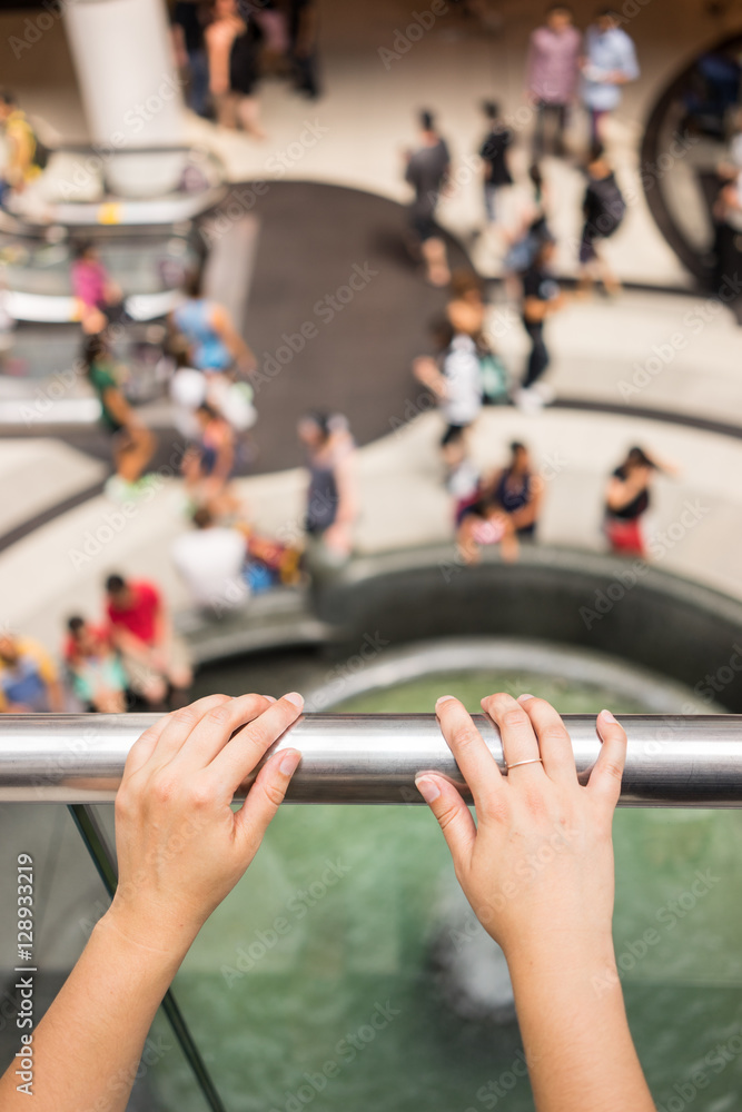 Point of view of a female standing on a second floor of a shopping mall looking down. Two hands visible in the frame. Point of view of a female standing on a second floor of a shopping mall looking down. Two hands visible in the frame.