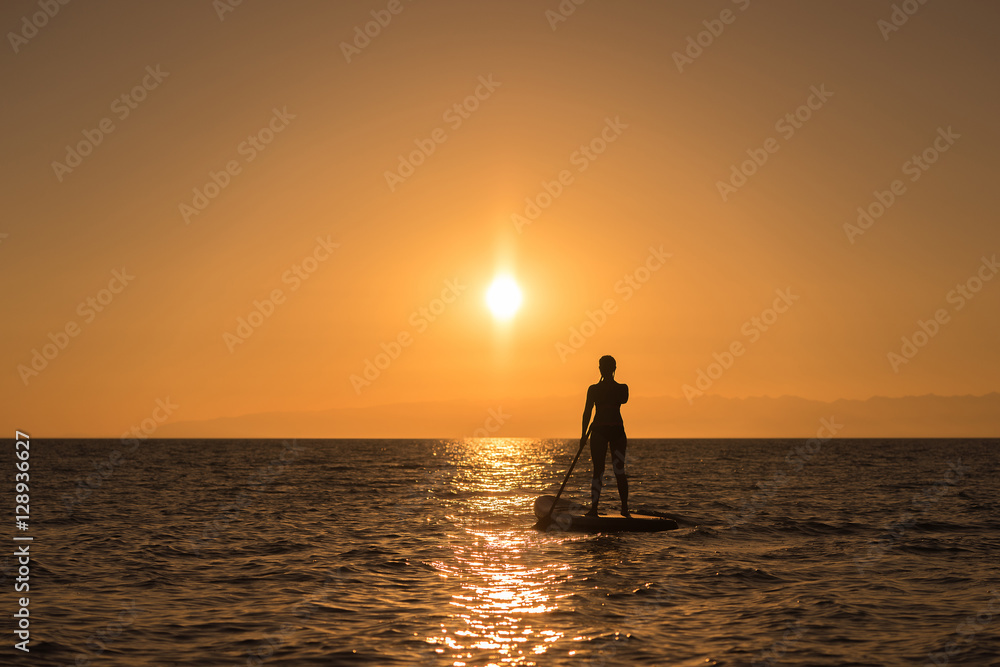 woman silhouette at paddle board in sunset