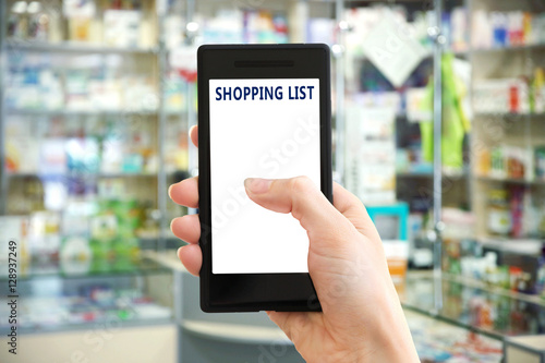 Woman with smartphone in store, closeup. Text SHOPPING LIST on screen.