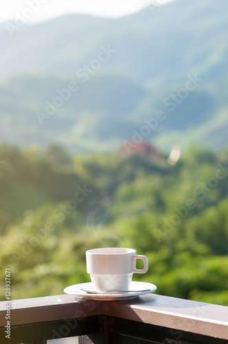 White cup of hot coffee on balcony with natural and mountains.