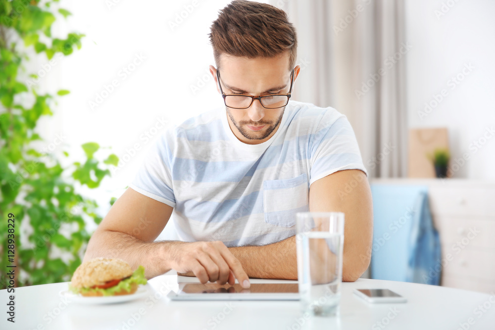 Young man having snack while working with tablet computer in kitchen Young man having snack while working with tablet computer in kitchen