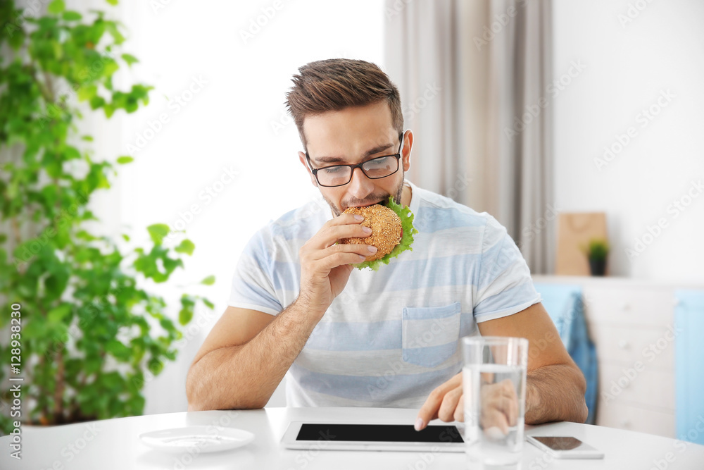 Young man having snack while working with tablet computer in kitchen Young man having snack while working with tablet computer in kitchen