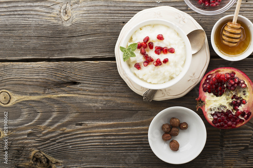 Fragrant warm homemade rice milk porridge with sugar and pomegranate seeds on a wooden background. The concept of healthy, seasonal dishes