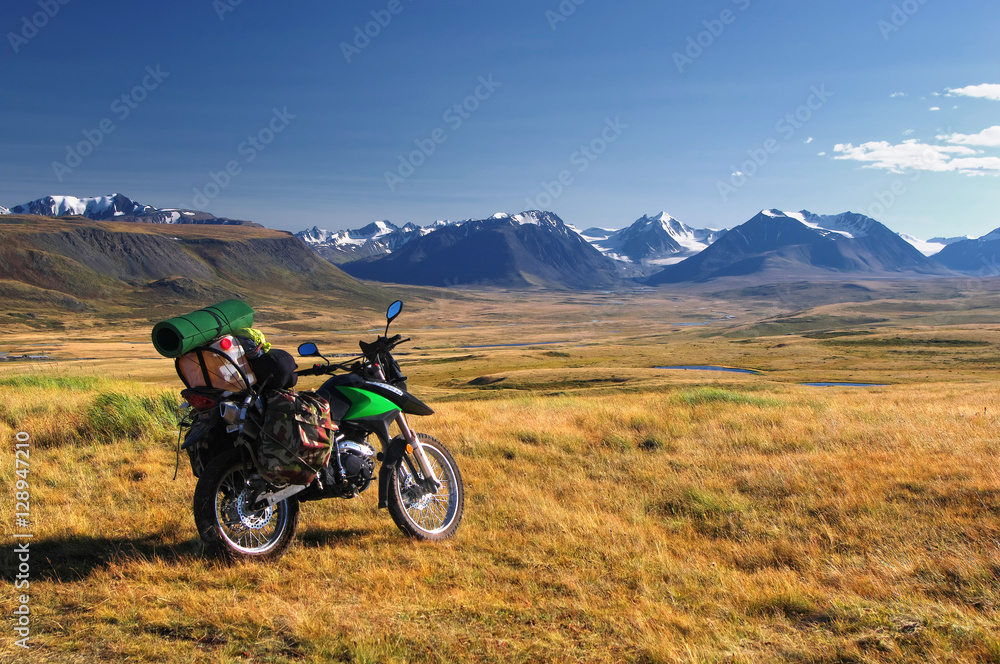 Enduro motorcycle traveler alone under a blue sky with white clouds on a background of mountain valley with  snow ice covered peaks and glaciers, Plateau Ukok, Altai, Siberia, Russia.