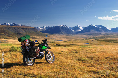 Enduro motorcycle traveler alone under a blue sky with white clouds on a background of mountain valley with snow ice covered peaks and glaciers, Plateau Ukok, Altai, Siberia, Russia.
