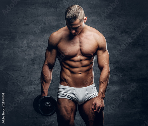 A man in a white panties holds dumbbell on grey background.