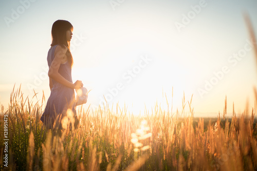 Beautiful girl in stylish summer dress walking in the field with flowers in sunlight,enjoying freedom feeling happy at sunset photo