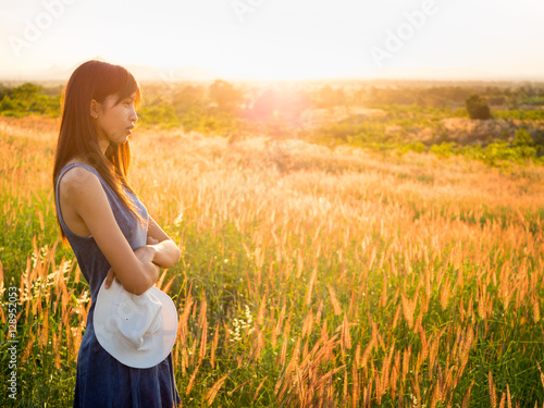 Beautiful girl in stylish summer dress walking in the field with flowers in sunlight,enjoying freedom feeling happy at sunset