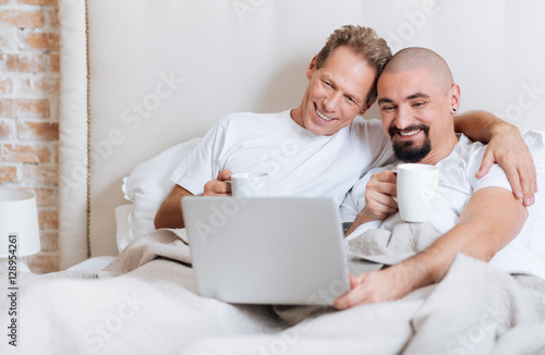 Delighted gay couple using the laptop in the bedroom