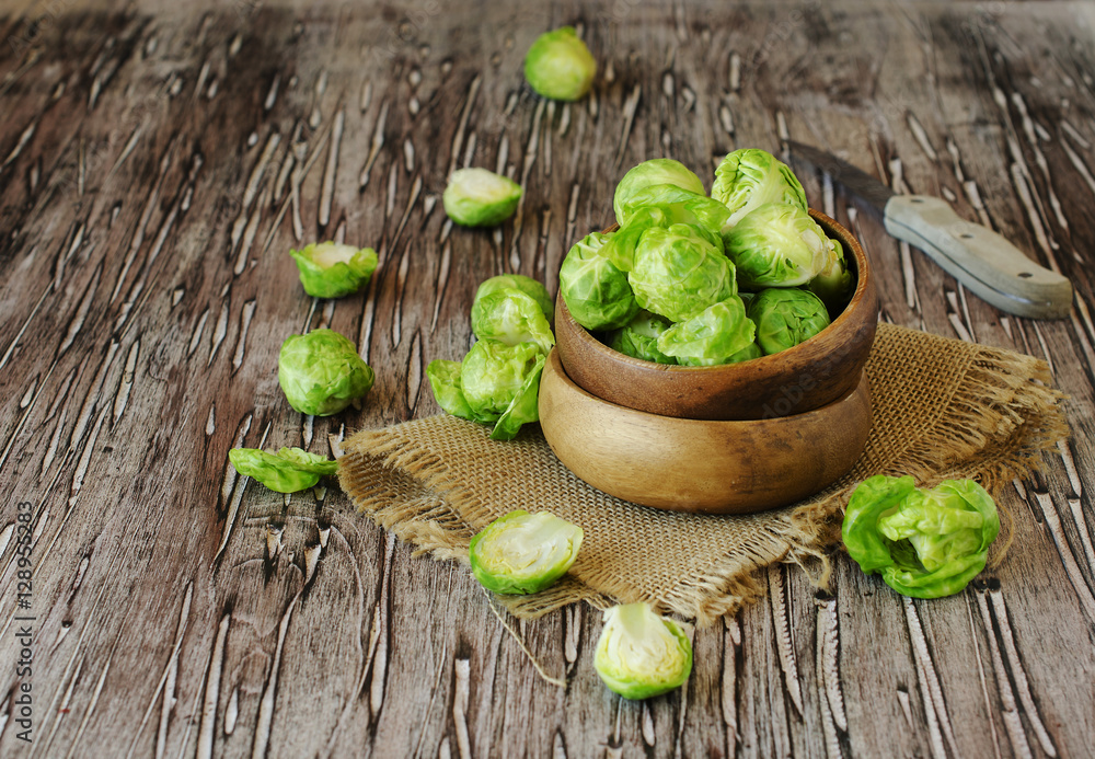Fototapeta Green raw Brussels sprouts in wooden bowl , selective focus