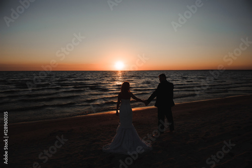 young couple stands at the sea beach looking at sunset