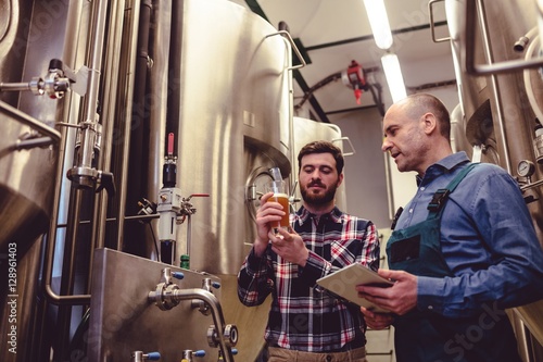 Owner inspecting beer with worker at brewery photo