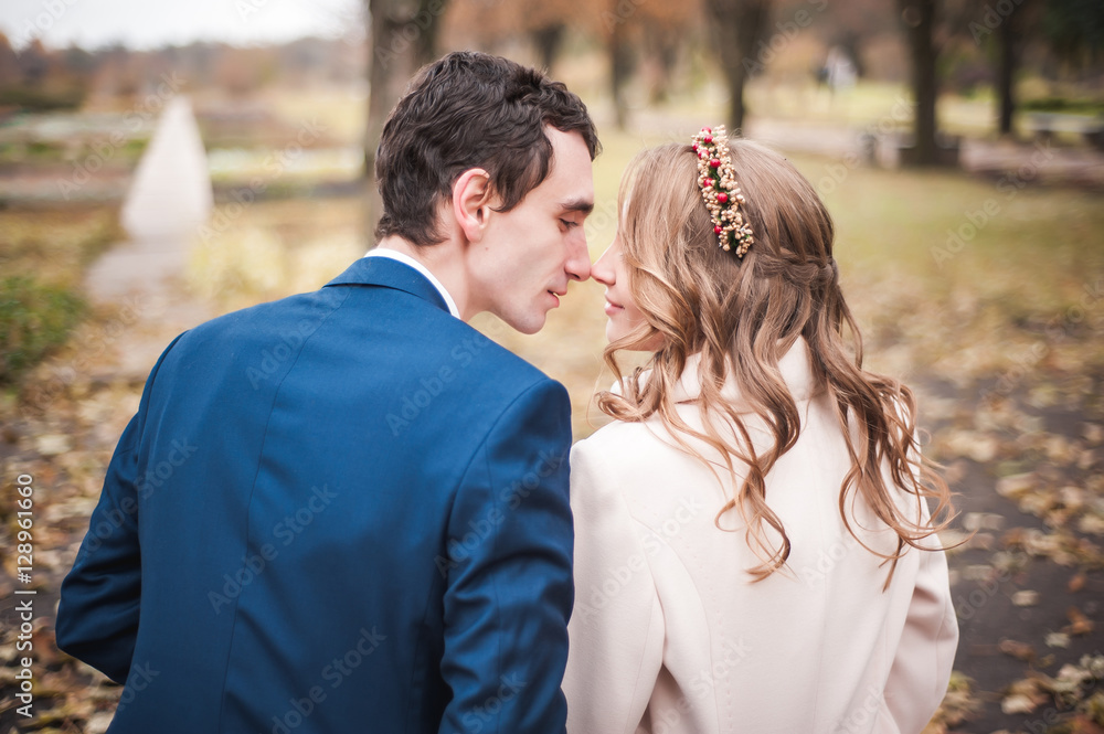 Naklejka premium Newlyweds sit on the wooden bench in an autumn garden, back view