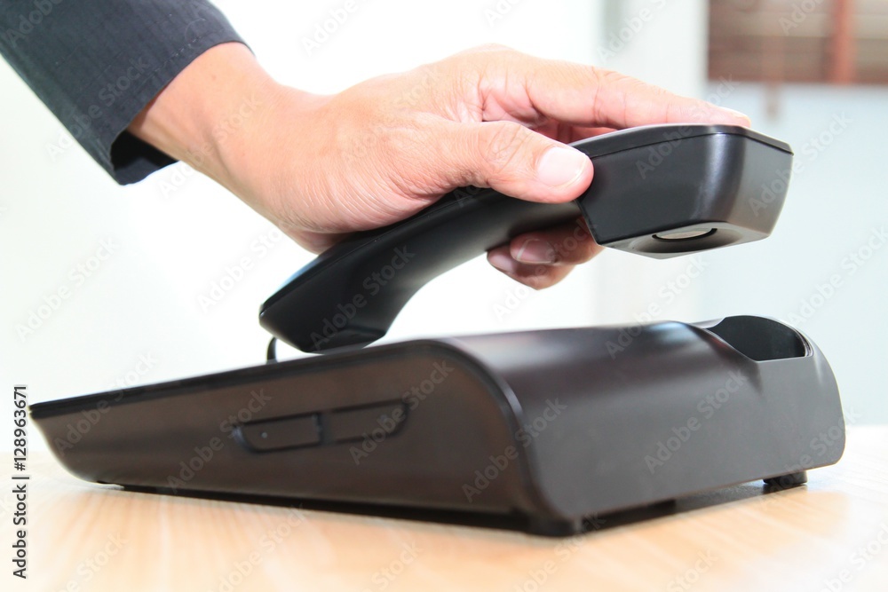 Fototapeta premium Closeup of a male hand holding phone receiver over telephone.