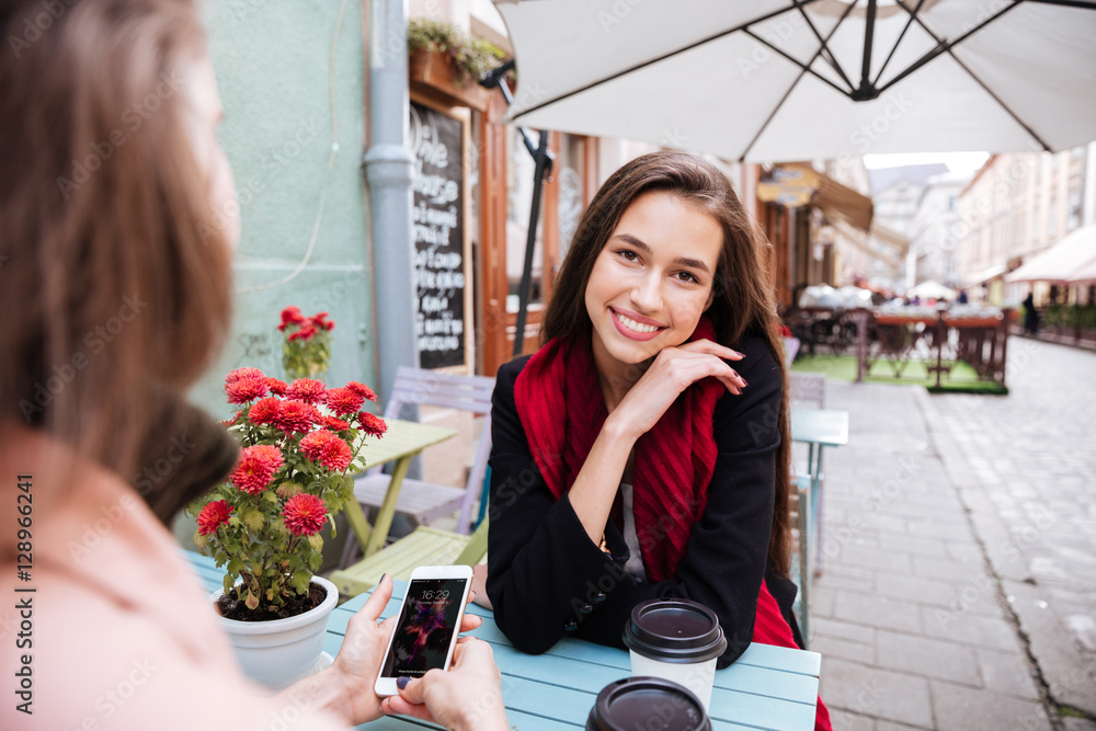 Two women talking and using cell phone in outdoor cafe Two women talking and using cell phone in outdoor cafe
