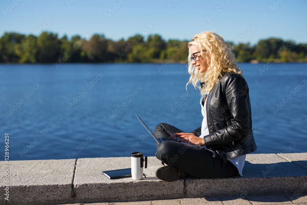 Woman sitting by the water and working on computer