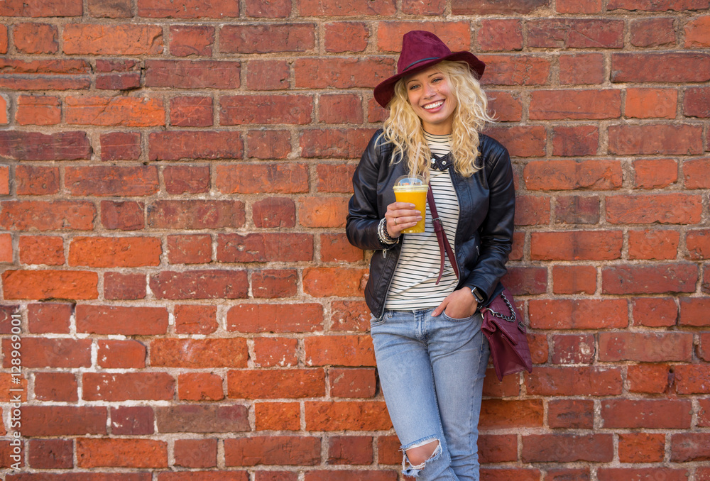 Modern woman standing by the brick wall with orange juice in her hands Modern woman standing by the brick wall with orange juice in her hands