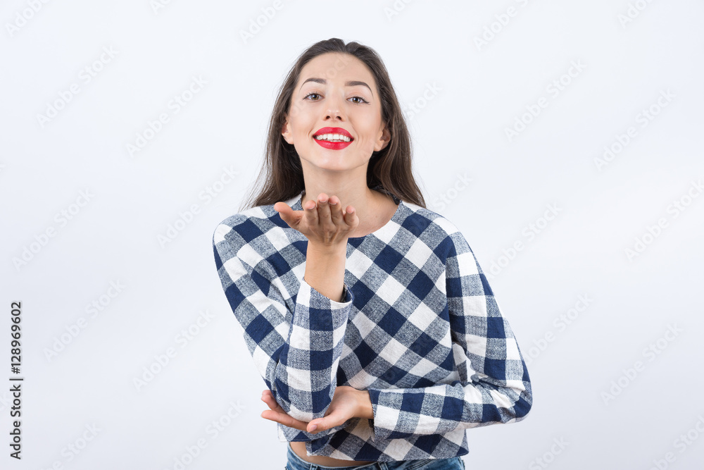 Young woman blowing while sending an air kiss against a white ba Young woman blowing while sending an air kiss against a white ba