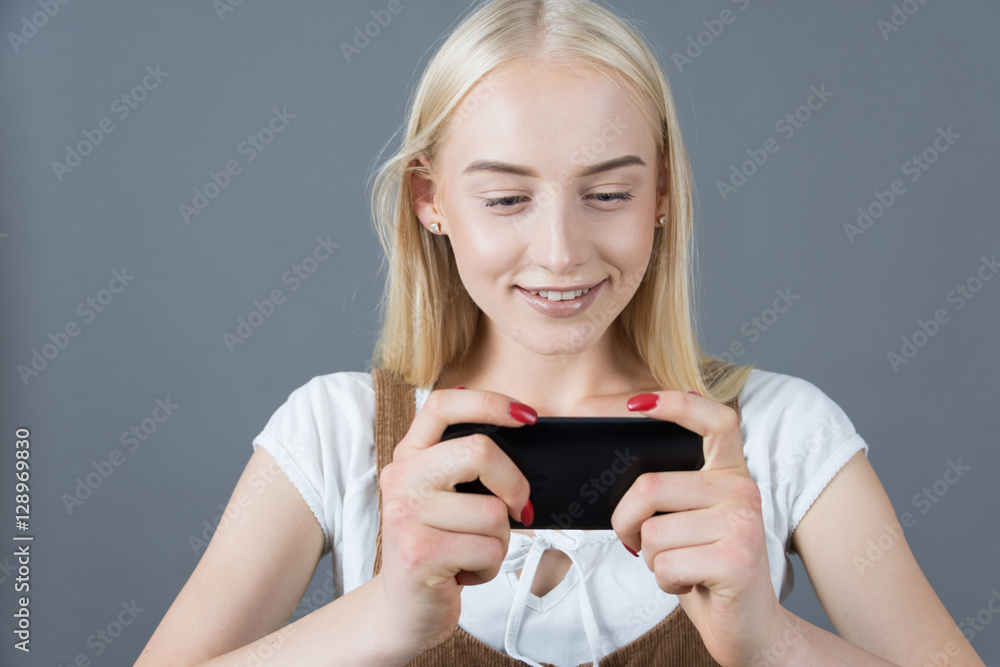 blonde schoolgirl playing a game on your phone, studio gray back blonde schoolgirl playing a game on your phone, studio gray back